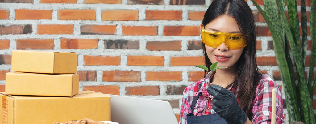 selling-plant-online-woman-holding-pot-plant-using-laptop