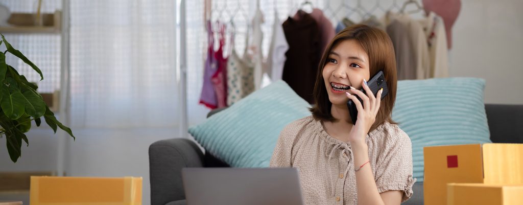 smiling-happy-young-asian-woman-entrepreneur-receiving-phone-call-new-sales-order-among-boxes-product-with-laptop-computer